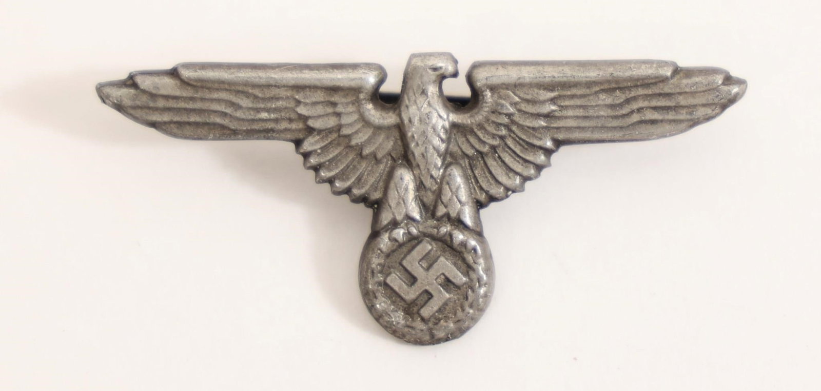 WWII German Eagle & Swastika Cap Badge: World War II German metal cap badge featuring spread-wing eagle clutching a wreath with swastika. Shows age, wear, and patina consistent with period use.