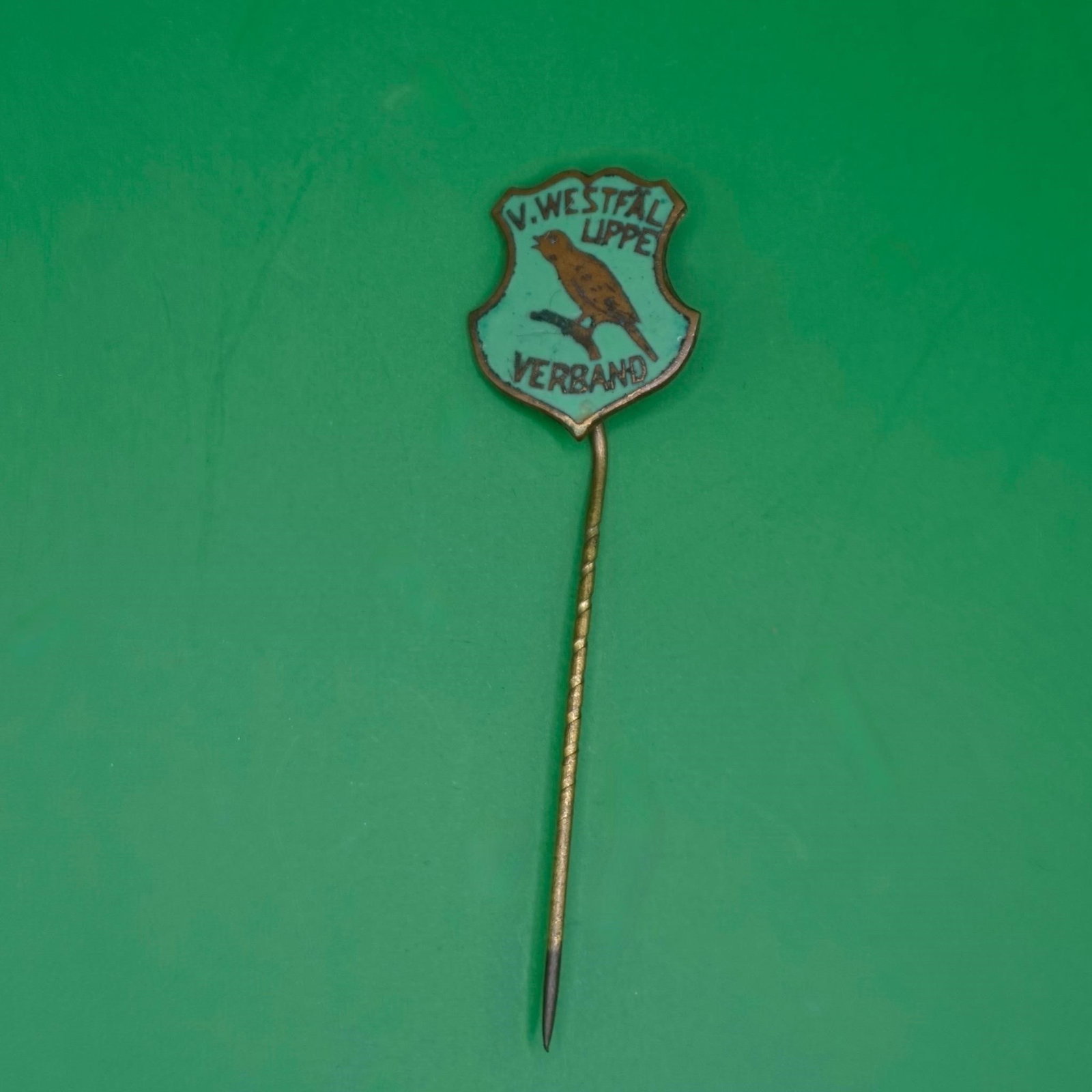 Vintage V. Westfal Lippe Verband Enamel Stick Pin: A small vintage enamel stick pin with a shield-shaped badge at the top. It has a light turquoise background, a brown bird perched on a branch in the center, and black text reading "V. WESTFAL LIPPE" a