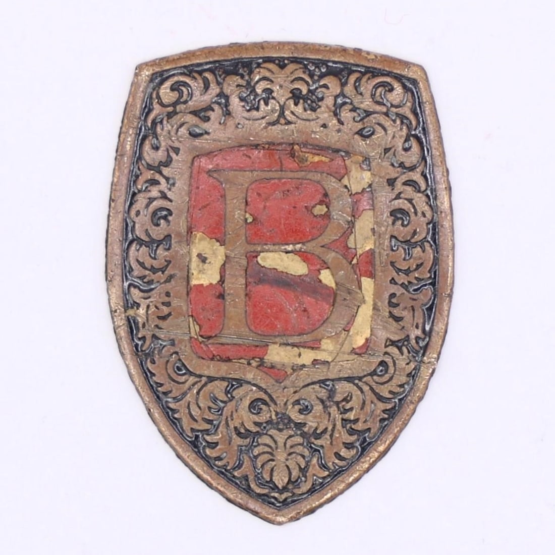 German Metal Shield Badge "B": This is a small metal shield badge with ornate scrollwork and a prominent red "B" at the center. The design suggests it was a decorative or uniform-style emblem, likely representing an organization, s