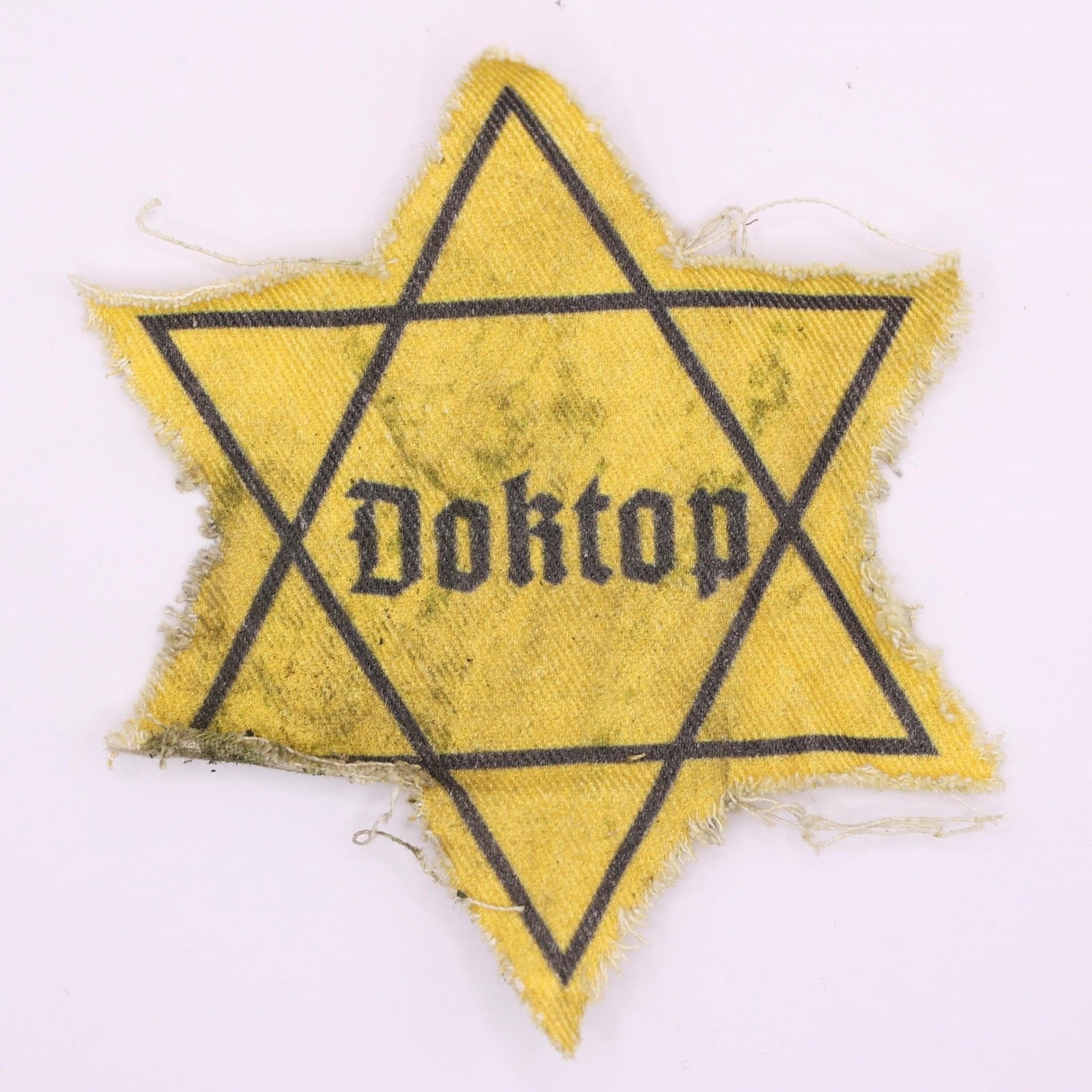 WWII Jewish Ghetto Star Patch "Doktop": World War II-era Jewish identification badge in the form of a yellow Star of David with the inscription "Doktop." Cloth patch worn on clothing during the Nazi occupation to identify Jewish