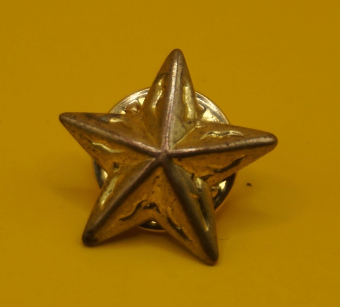 Gold-Tone, Three-Dimensional Star Lapel Pin: It is a five-pointed star design, likely made of iron or a similar base metal and plated with gold. The pin is similar in appearance to military insignia, such as the U.S. Army's World War II era star