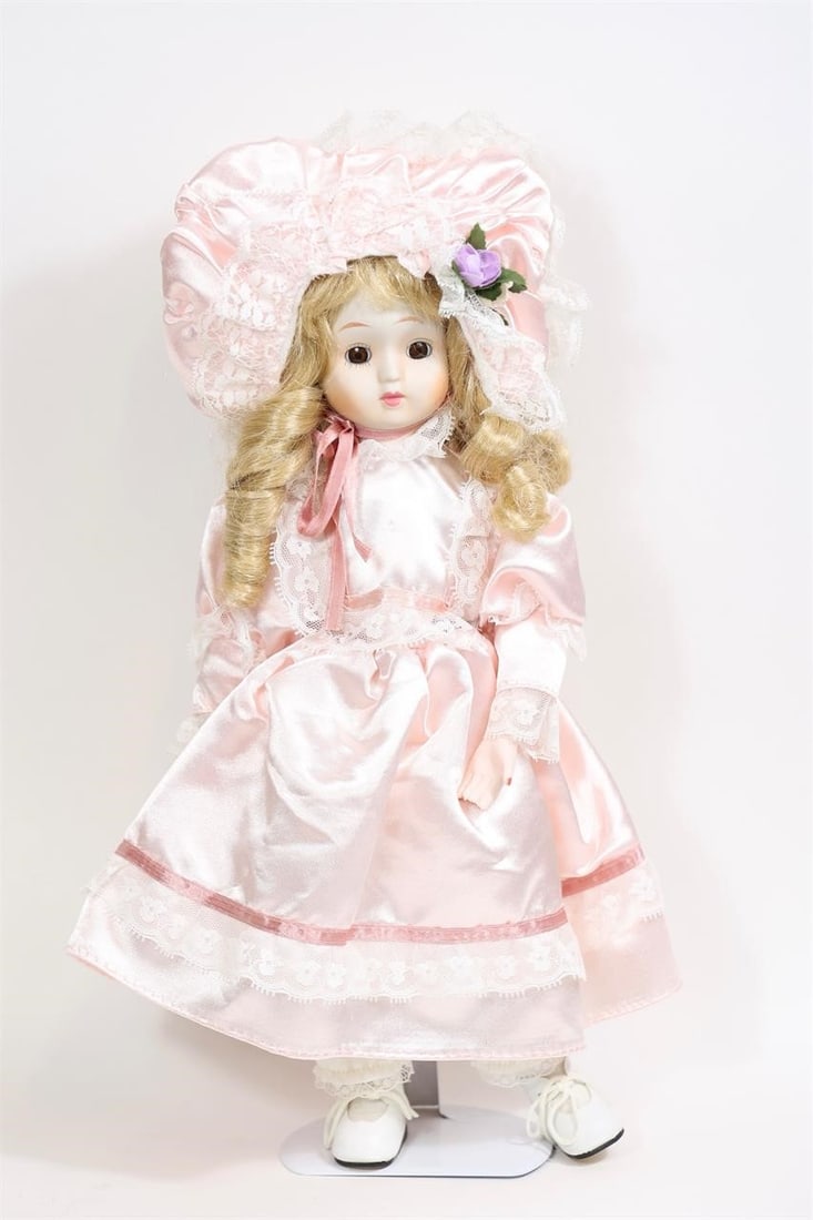 Vintage Porcelain Doll in Pink Satin Dress: Vintage porcelain doll featuring a porcelain head, hands, and feet with a soft cloth body. The doll has blonde curled hair and is dressed in a pink satin-style dress with lace trim, matching bonnet,