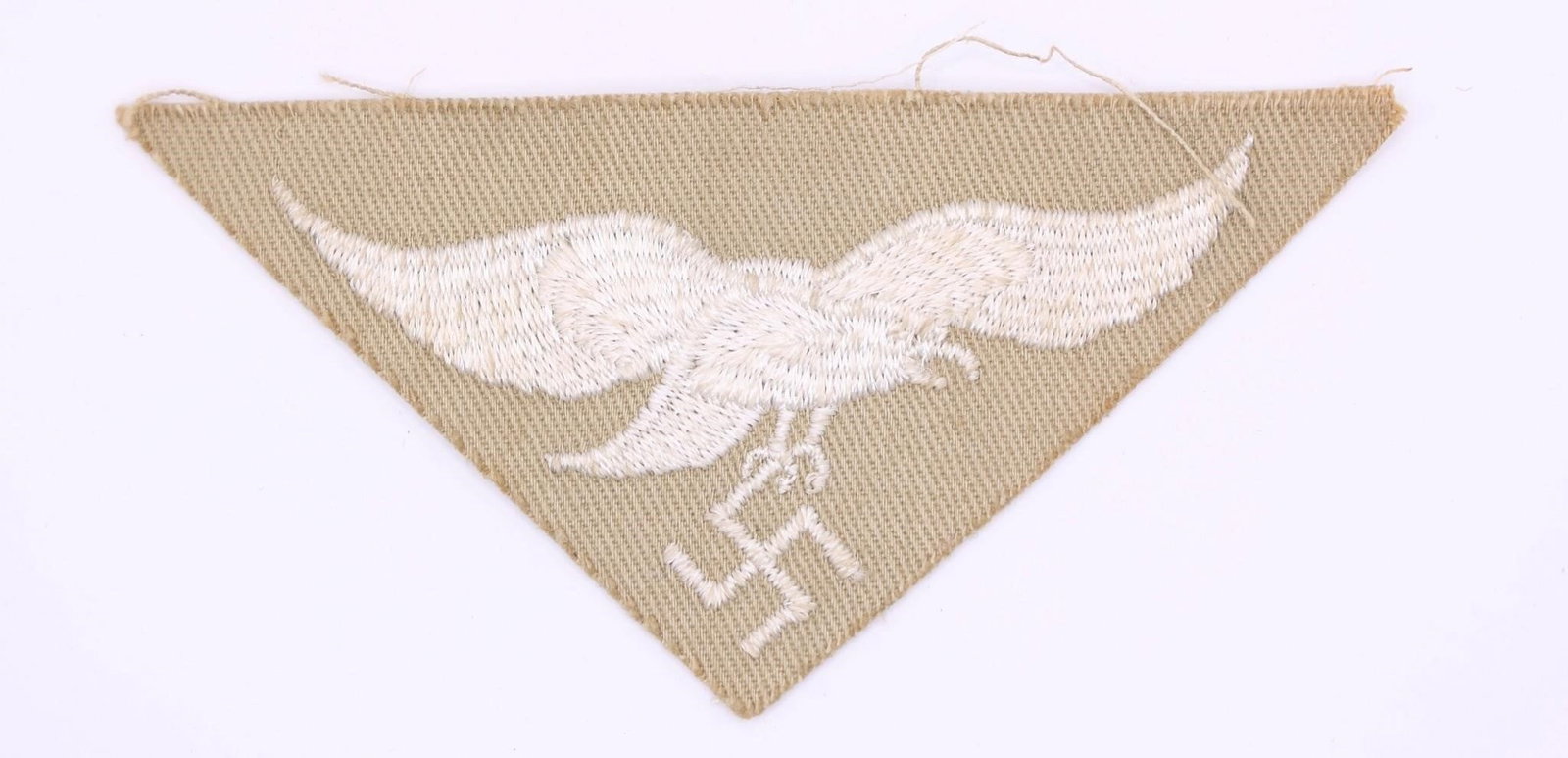 Luftwaffe Africa Corps Tropical Eagle: Machine-embroidered second pattern eagle (circa 1936-1945) in silvery-grey cotton threads on a cut-out, inverted triangular tan cotton base. Measures approximately 83 mm wingspan from tip to tip.
