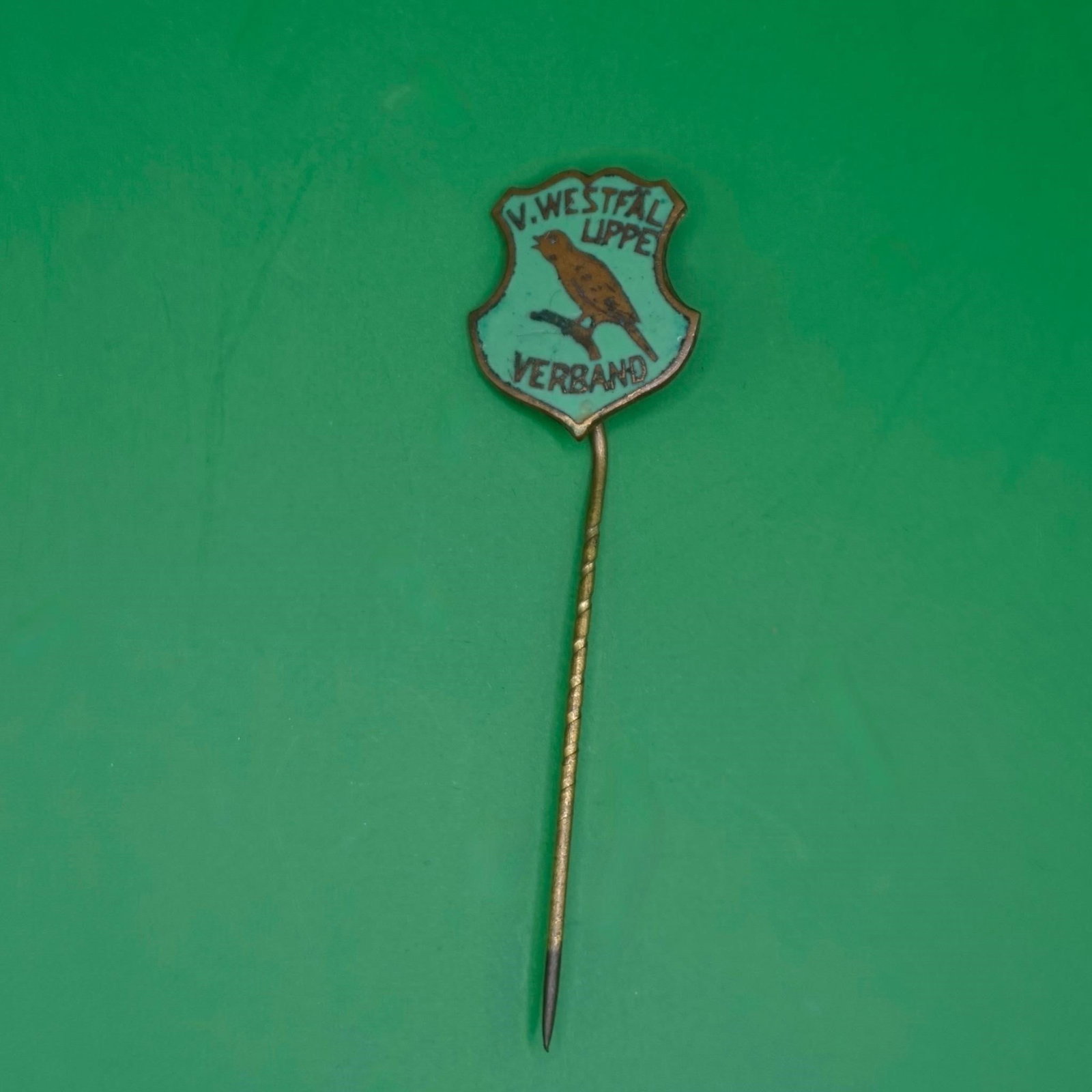 Vintage V. Westfal Lippe Verband Enamel Stick Pin: A small vintage enamel stick pin with a shield-shaped badge at the top. It has a light turquoise background, a brown bird perched on a branch in the center, and black text reading "V. WESTFAL LIPPE" a