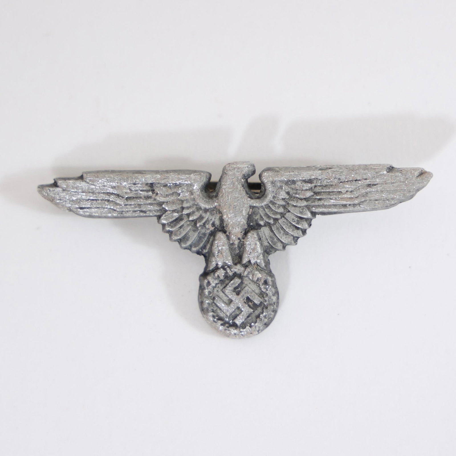 WWII German Wehrmacht Eagle Cap Insignia: Vintage German Wehrmacht eagle insignia from World War II era, featuring spread-wing eagle clutching wreath and swastika, worn on military visor caps, collectible historical militaria piece.