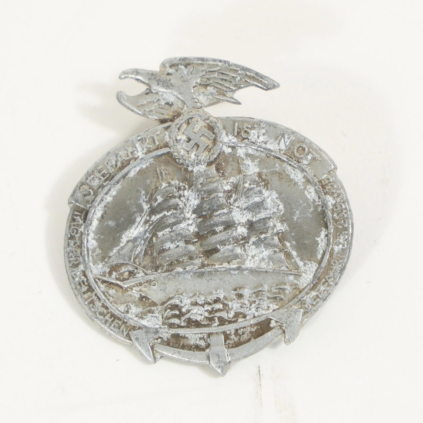 German National Sea Travel Day Badge: A lightweight metal event badge showing a three-masted sailing ship over waves, topped by an eagle clutching emblem. The front ring carries the event inscription, and the back has a simple pin fastene