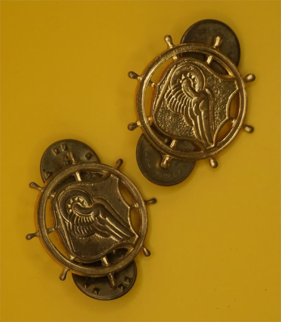 WWII US Army Corps Officer Branch Insignia Pins: This is a pair of US Army Transportation Corps officer branch insignia pins. The insignia features a ship's steering wheel (mariner's helm), superimposed on a shield with a winged car wheel on a