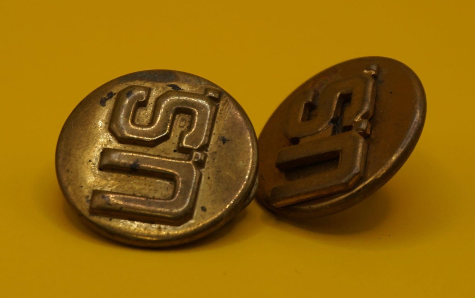 WWII Vintage US Military Brass Collar Insignia Pin: These are vintage US military brass collar insignia pins. They feature the letters "US" and were typically worn on the collar of a dress uniform. The pins are made of brass and show signs of tarnish a