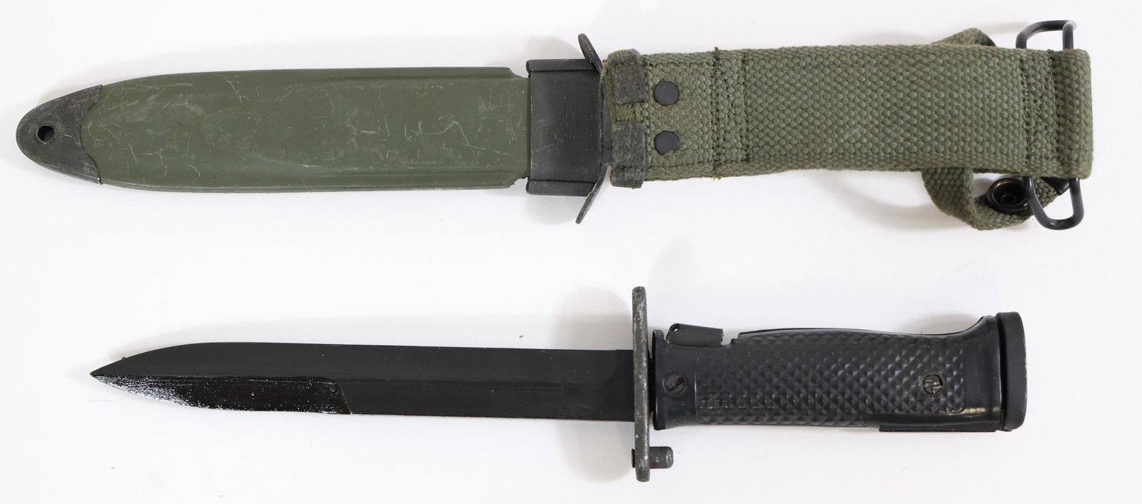 Military-Style Bayonet w/ Scabbard - 11.5" OAL: Military-style bayonet featuring a straight blade, textured black grip scales with rivets, and metal guard with mounting mechanism. Includes olive drab scabbard with canvas hanger and metal fittings. 