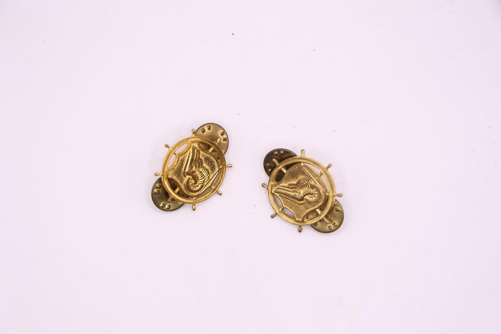 WWII US Army Corps Officer Branch Insignia Pins: This is a pair of US Army Transportation Corps officer branch insignia pins. The insignia features a ship's steering wheel (mariner's helm), superimposed on a shield with a winged car wheel on a