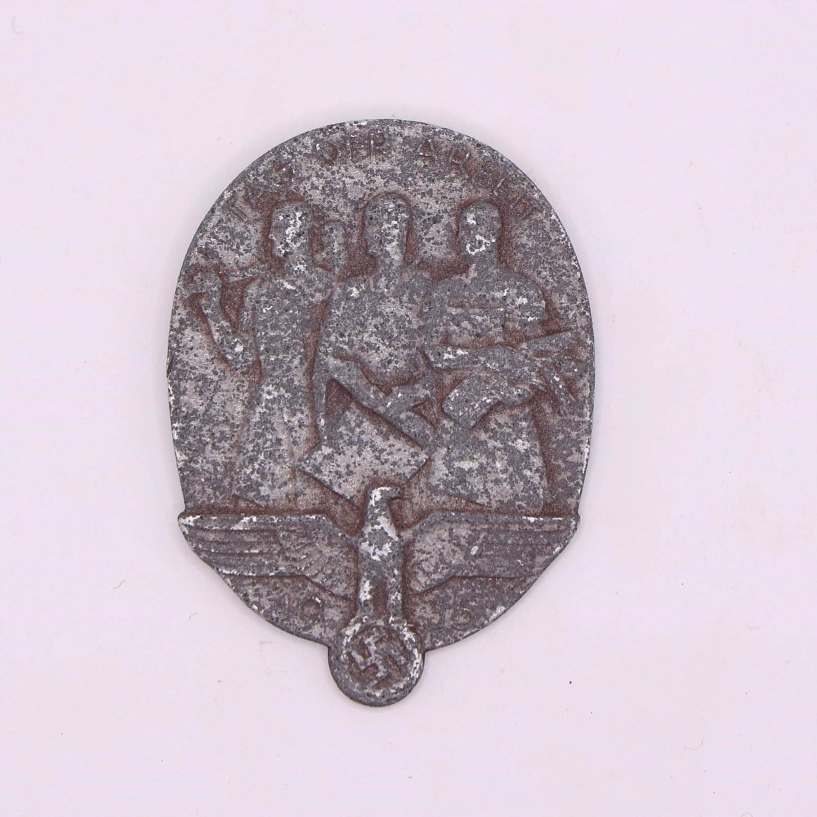 1935 "Tag der Arbeit" Labor Badge: An oval 1935 labor-day badge featuring three standing figures-a worker with a hammer, a man holding a rolled document, and a woman with a bundle of wheat. Below them is an eagle above the date "1935"