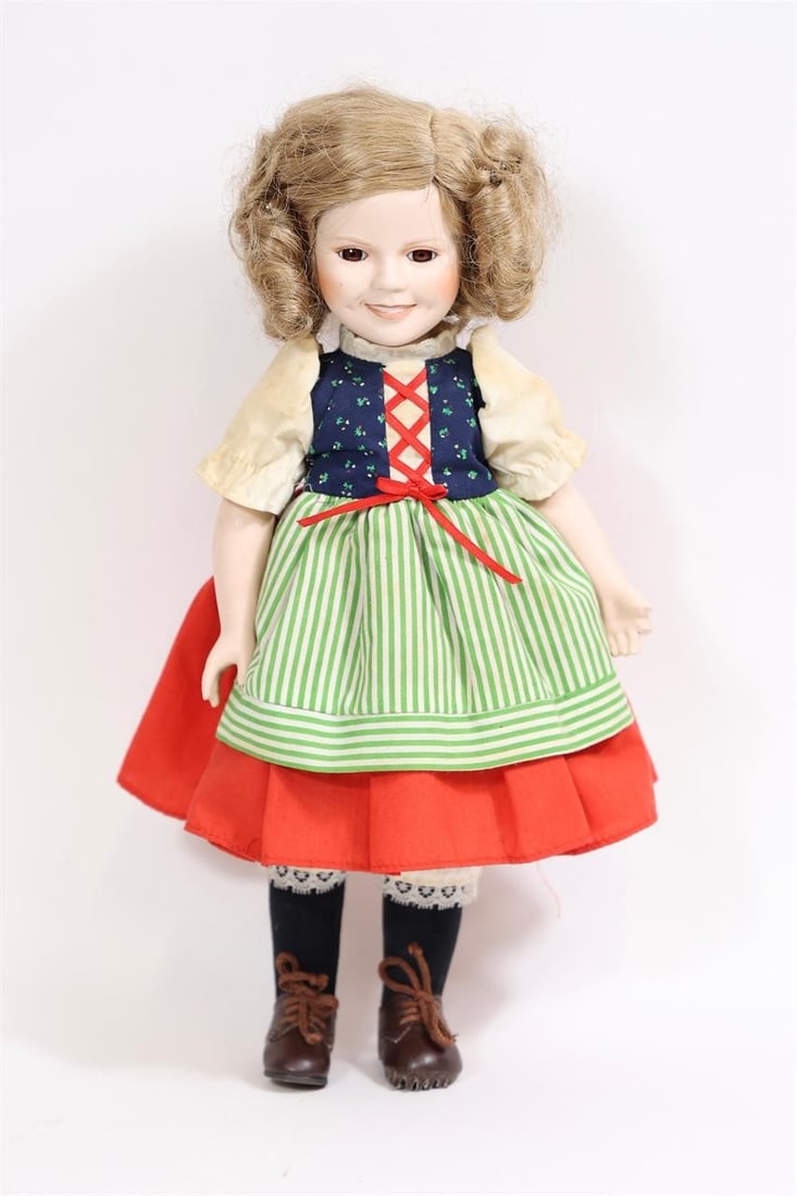 Shirley Temple Porcelain Doll in Traditional Dress: Vintage Shirley Temple porcelain doll featuring a detailed traditional-style outfit with layered skirt, apron, and lace trim. Doll has a porcelain head, hands, and lower legs with a soft cloth body.