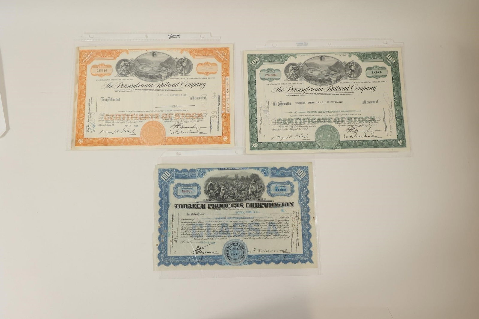 Pennsylvania Railroad & Tobacco Stocks: Collection of three vintage stock certificates including two Pennsylvania Railroad Company certificates and one Tobacco Products Corporation certificate. Features engraved designs, company seals,