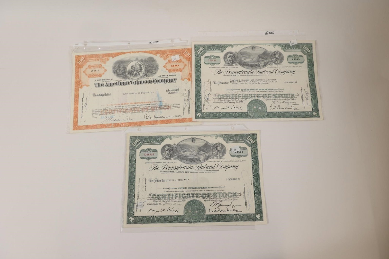 American Tobacco & Railroad Stocks: Group of three vintage stock certificates including one American Tobacco Company common stock certificate and two Pennsylvania Railroad Company certificates. Features engraved artwork, original