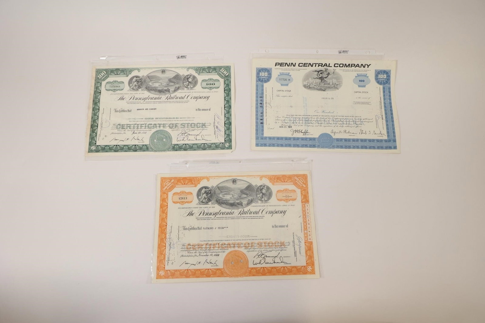 3 Railroad & Penn Central Stock Certificates: Group of three vintage stock certificates including two Pennsylvania Railroad Company certificates and one Penn Central Company certificate. Features engraved railroad-themed artwork, corporate