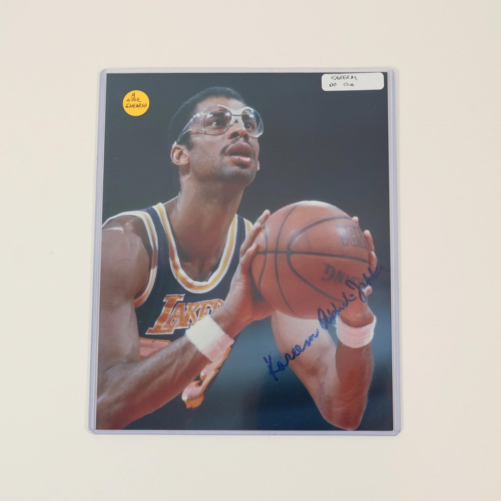 Kareem Abdul-Jabbar Signed Lakers Photo: Autographed color photograph of Kareem Abdul-Jabbar in a Los Angeles Lakers uniform. Features a blue ink signature across the image and depicts the Hall of Fame center preparing a free throw. Housed