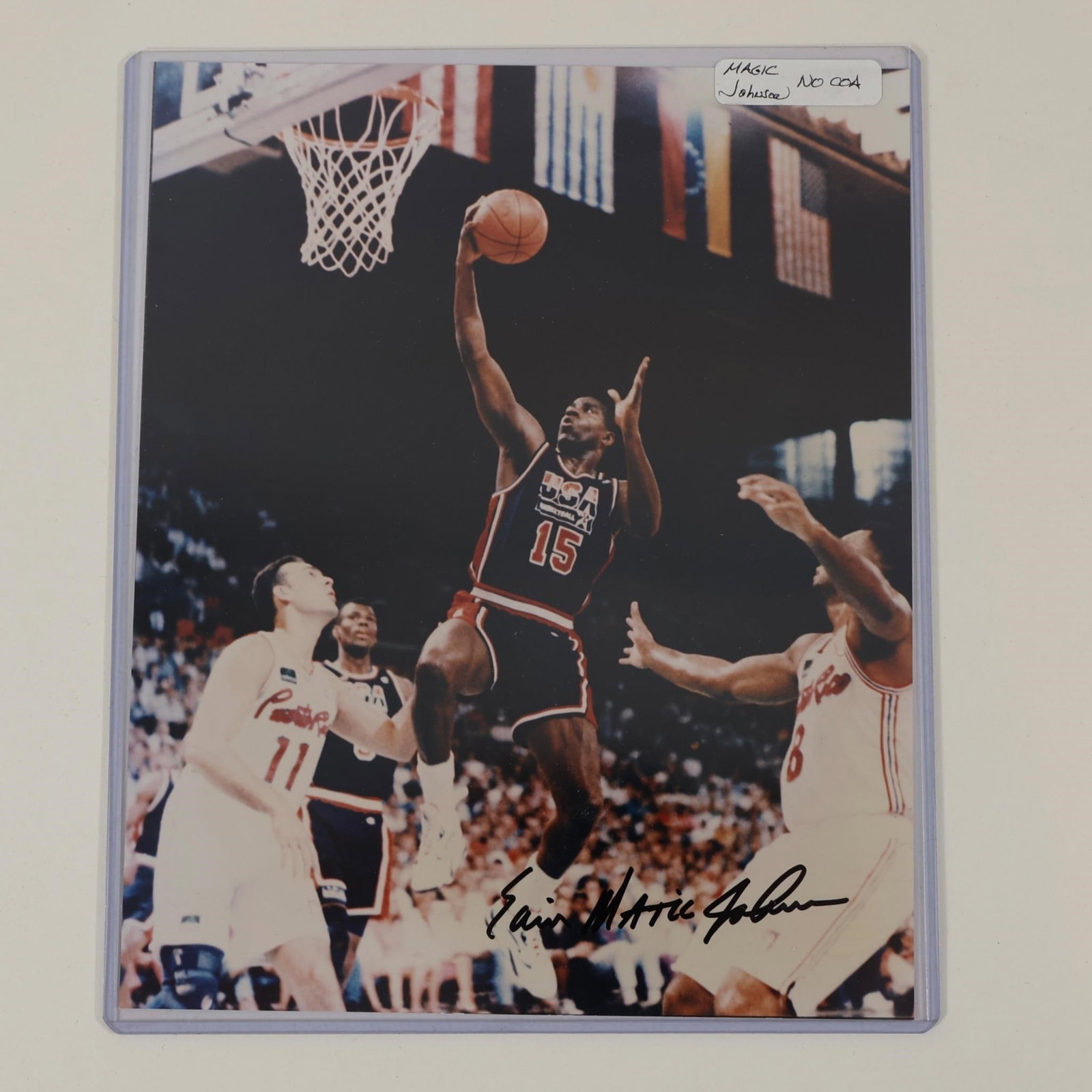 Earvin "Magic" Johnson Signed USA Basketball Photo: Autographed color photograph featuring Earvin "Magic" Johnson in a USA Basketball uniform during game action. Signature appears across the lower portion of the image. Presented in a protective sleeve.