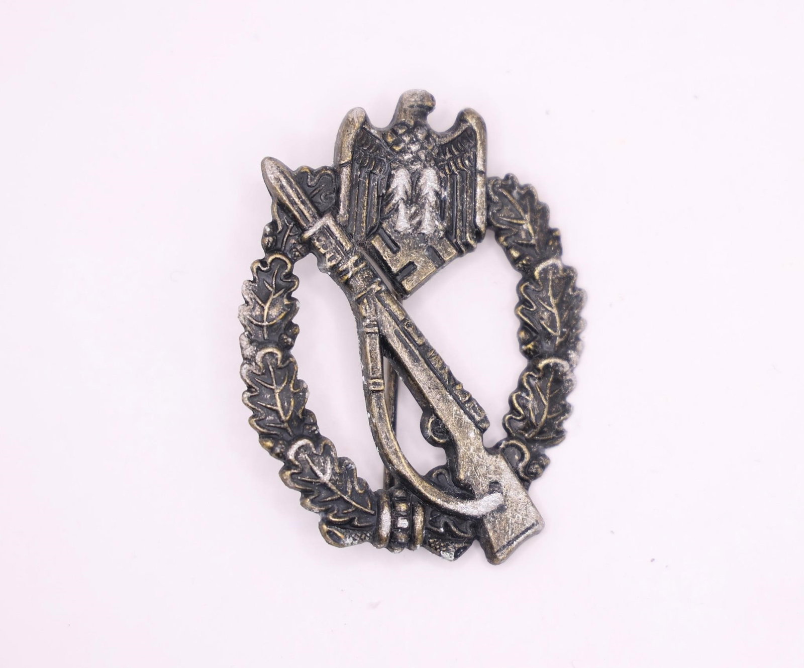 German WWII Infantry Assault Badge: German WWII Infantry Assault Badge (Infanterie-Sturmabzeichen), featuring the classic Mauser K98 rifle with bayonet overlaid on an oak leaf wreath. This late-war style badge displays detailed