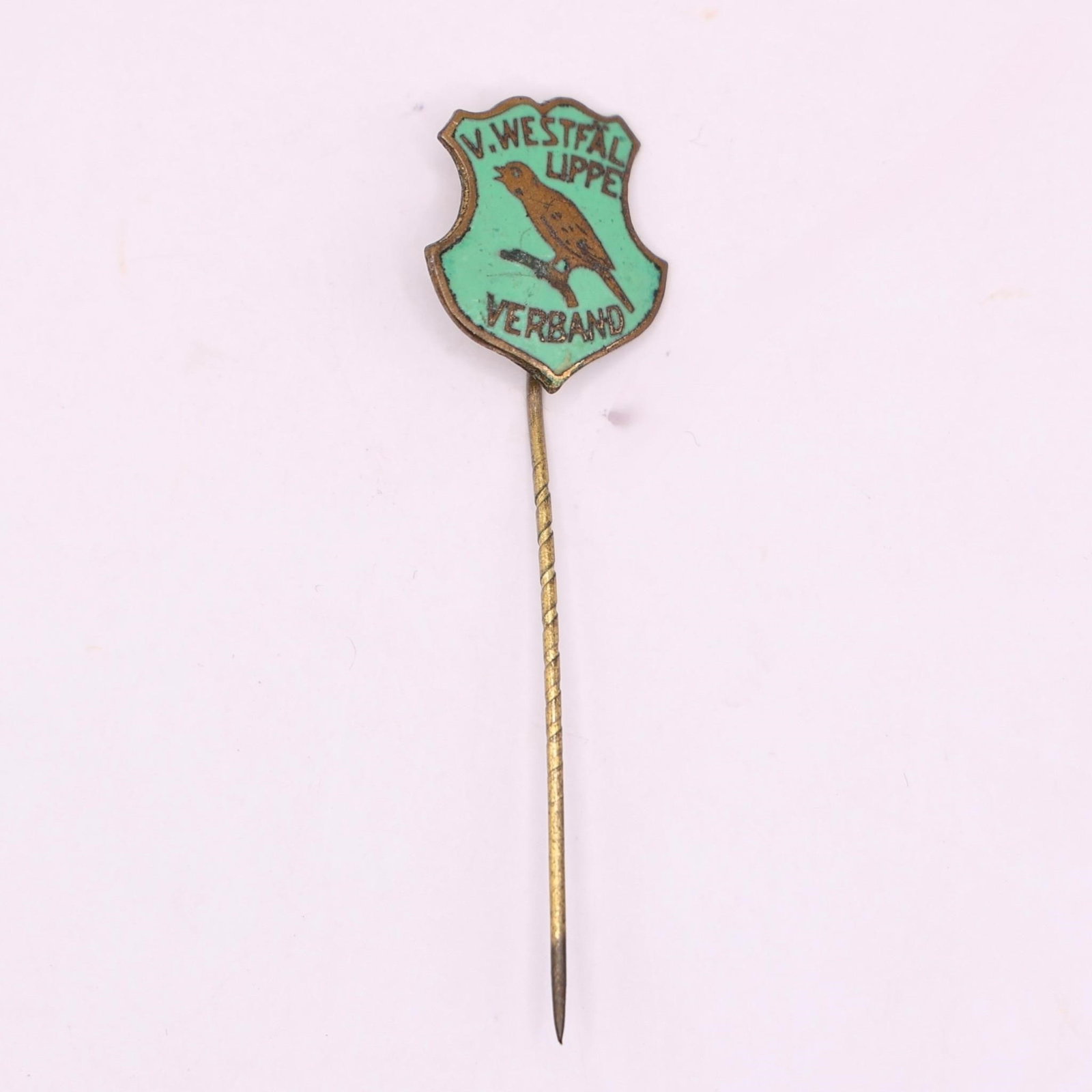 Vintage V. Westfal Lippe Verband Enamel Stick Pin: A small vintage enamel stick pin with a shield-shaped badge at the top. It has a light turquoise background, a brown bird perched on a branch in the center, and black text reading "V. WESTFAL LIPPE" a