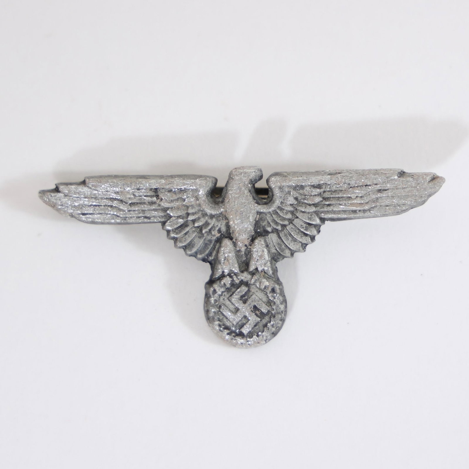 WWII German Wehrmacht Eagle Cap Insignia: Vintage German Wehrmacht eagle insignia from World War II era, featuring spread-wing eagle clutching wreath and swastika, worn on military visor caps, collectible historical militaria piece.