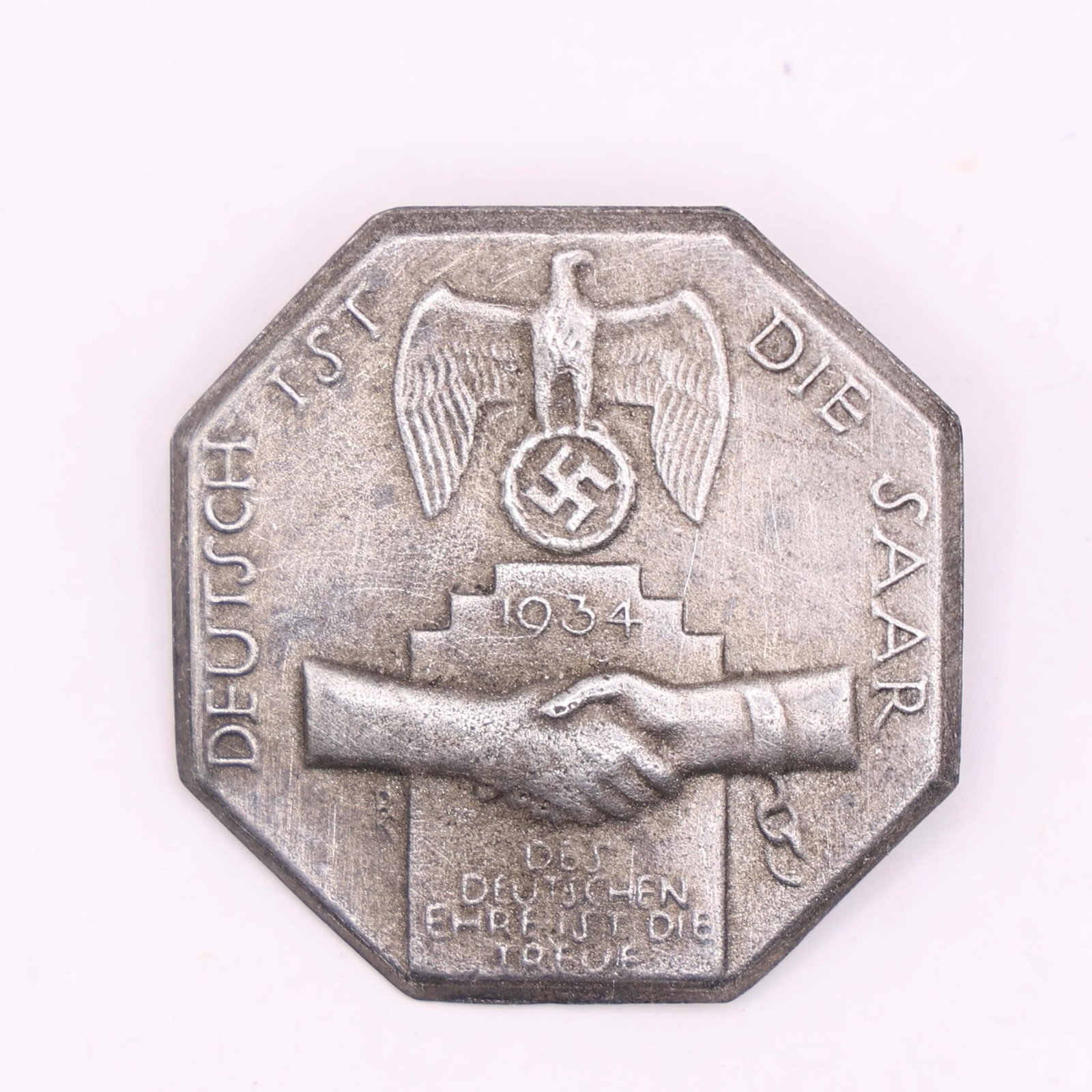 1934 NSDAP "Deutsch ist die Saar" Badge: Issued in 1934, this NSDAP badge commemorated the Saar region's return to Germany. It features an eagle clutching a wreathed swastika above two shaking hands, symbolizing unity and loyalty, and was wo