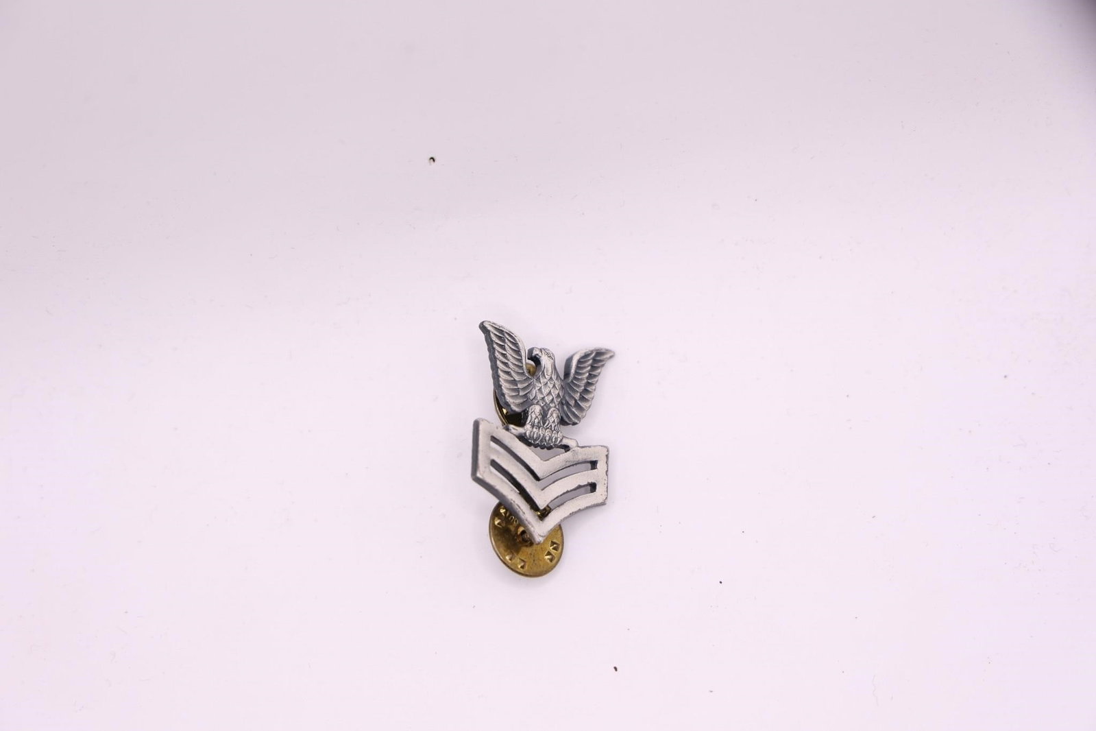 WWII US Navy PO1 E-6 Collar Insignia Pin: The insignia features an eagle with outstretched wings perched above three chevrons. It indicates the rank of Petty Officer First Class in the U.S. Navy. The pin appears to be made of a brushed or sat