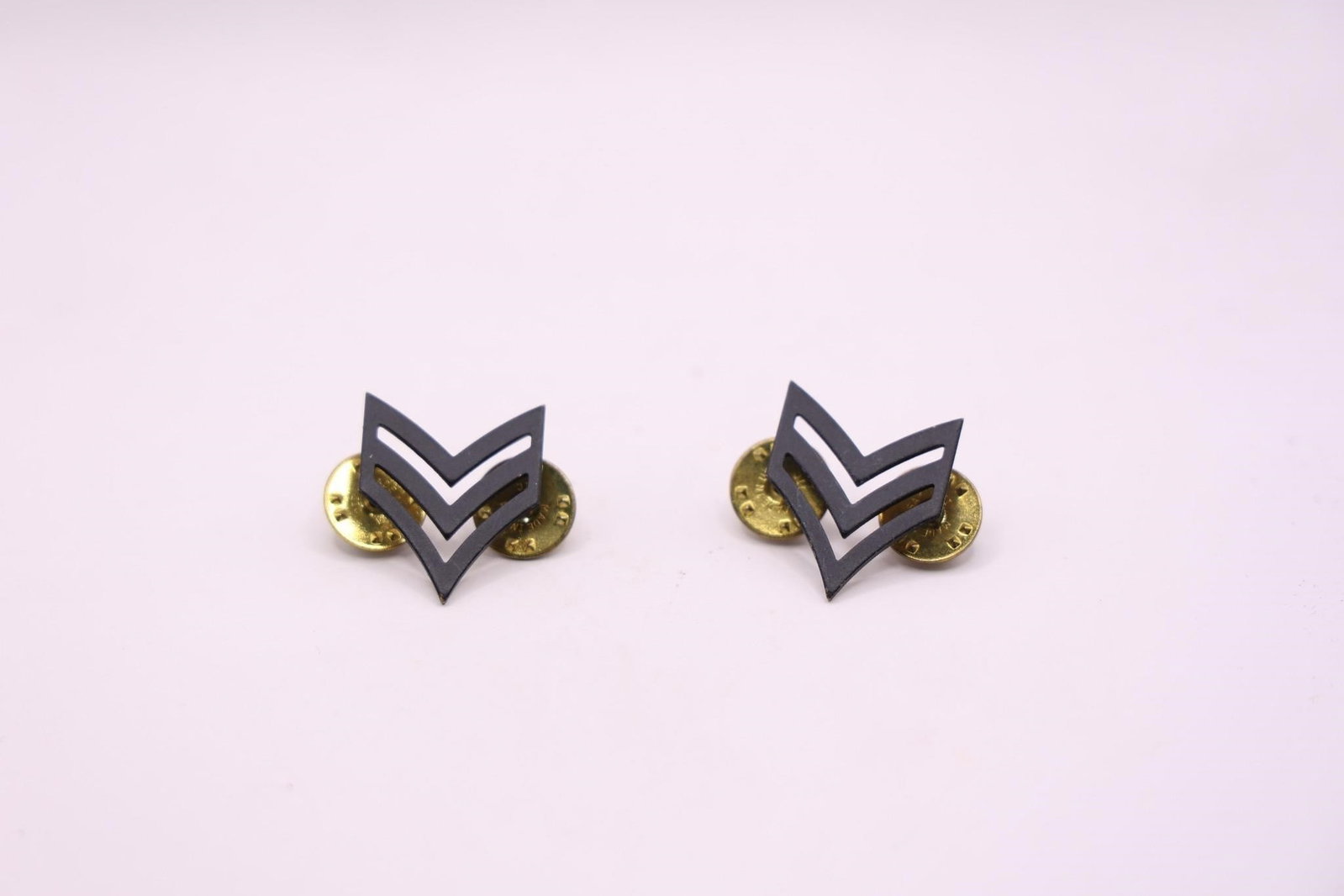 WWII US Army Sergeant Rank Insignia Pins: This is a pair of U.S. Army Sergeant rank insignia pins. The insignia features three chevrons, indicating the rank of Sergeant (E-5). The pins are a black metal, subdued design. They are authorized fo