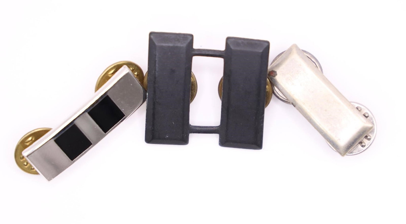 WWII US Army Captain Rank Insignia Pins: These are U.S. Army Captain rank insignia pins. The silver-colored pin on the left appears to be a worn or older version of the rank. The polished pin in the center is a standard, modern U.S. Army