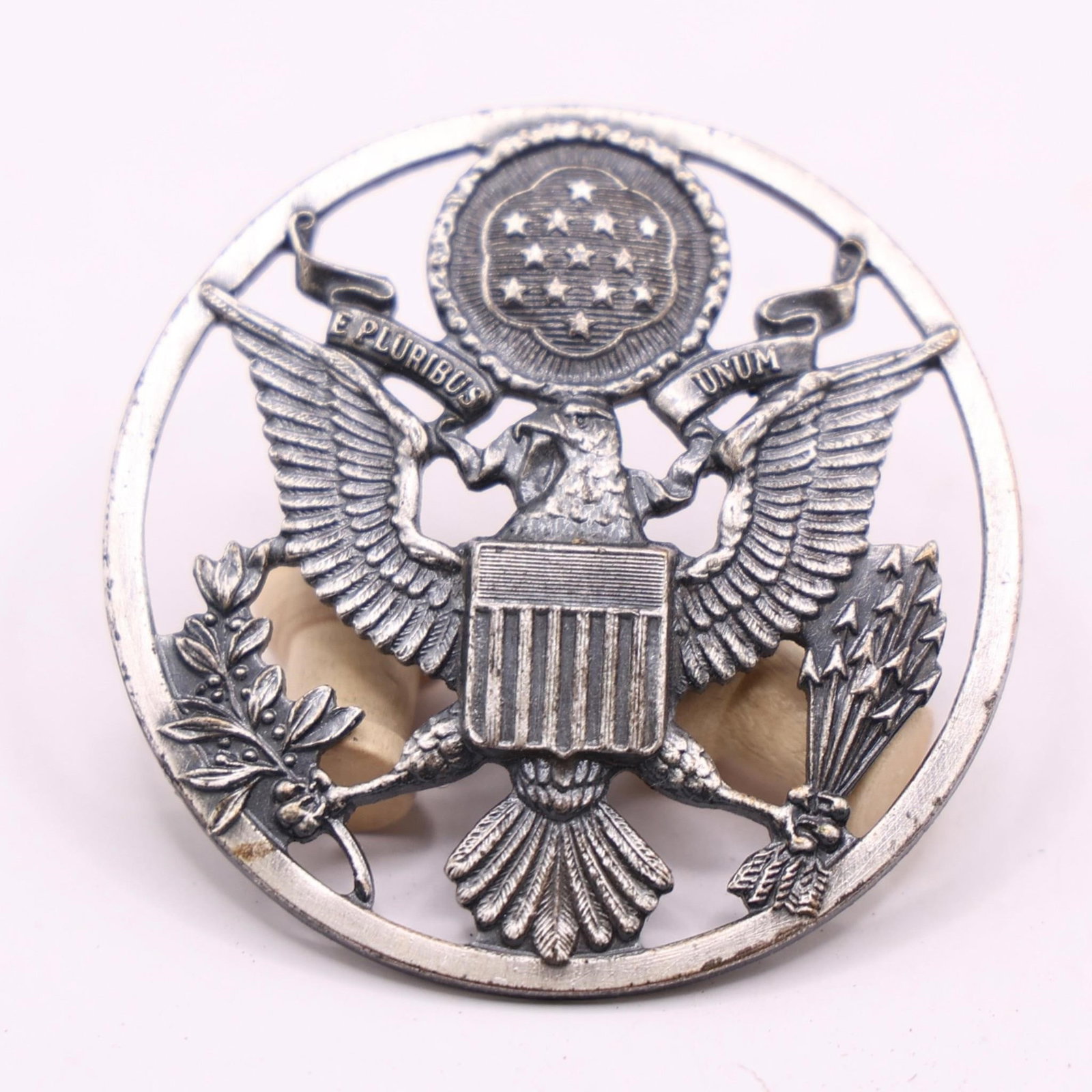 WWII USAF Enlisted Male Service Cap Device: This is a United States Air Force (USAF) enlisted male service cap device. It features the United States Coat of Arms enclosed within a ring. The ring distinguishes it from the officer's version,