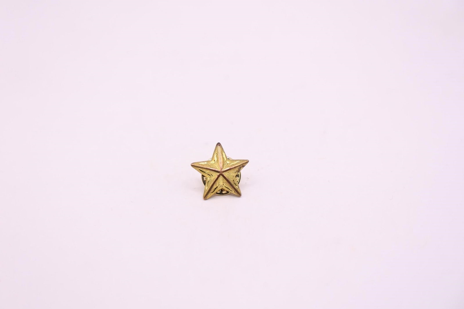 Gold-Tone, Three-Dimensional Star Lapel Pin: It is a five-pointed star design, likely made of iron or a similar base metal and plated with gold. The pin is similar in appearance to military insignia, such as the U.S. Army's World War II era star