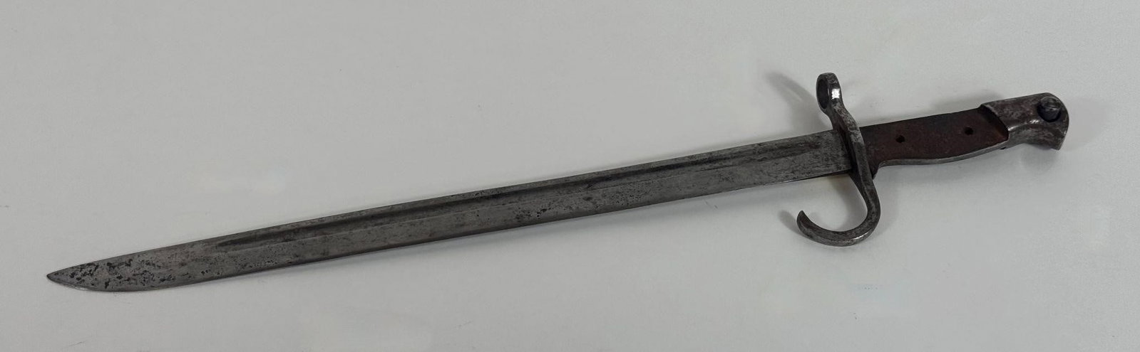 WWII Japanese Type 30 Arisaka Bayonet: The 40cm blade retains much of its original factory blued finish, showing wear consistent with age. It is marked on the ricasso and stamped with a serial number on the pommel. The three-sided cloverle