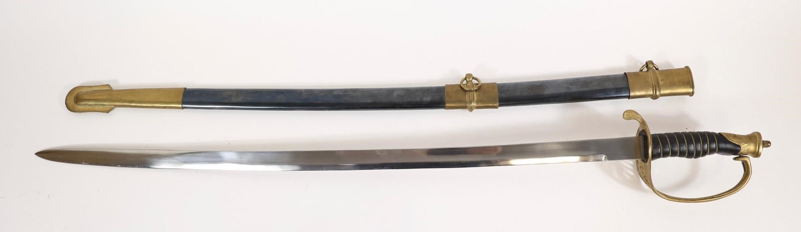US Style Cavalry Saber w/ Scabbard / decor: US-style cavalry saber featuring a curved blade, brass guard, and black grip with brass pommel. Includes metal scabbard with brass fittings and suspension rings. Approximate measurements: 37.5"