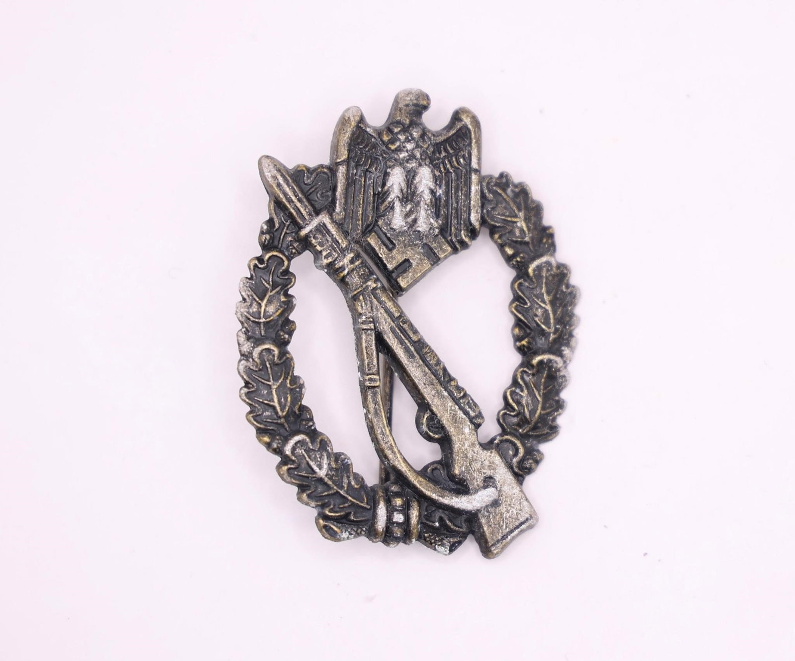 German WWII Infantry Assault Badge: German WWII Infantry Assault Badge (Infanterie-Sturmabzeichen), featuring the classic Mauser K98 rifle with bayonet overlaid on an oak leaf wreath. This late-war style badge displays detailed