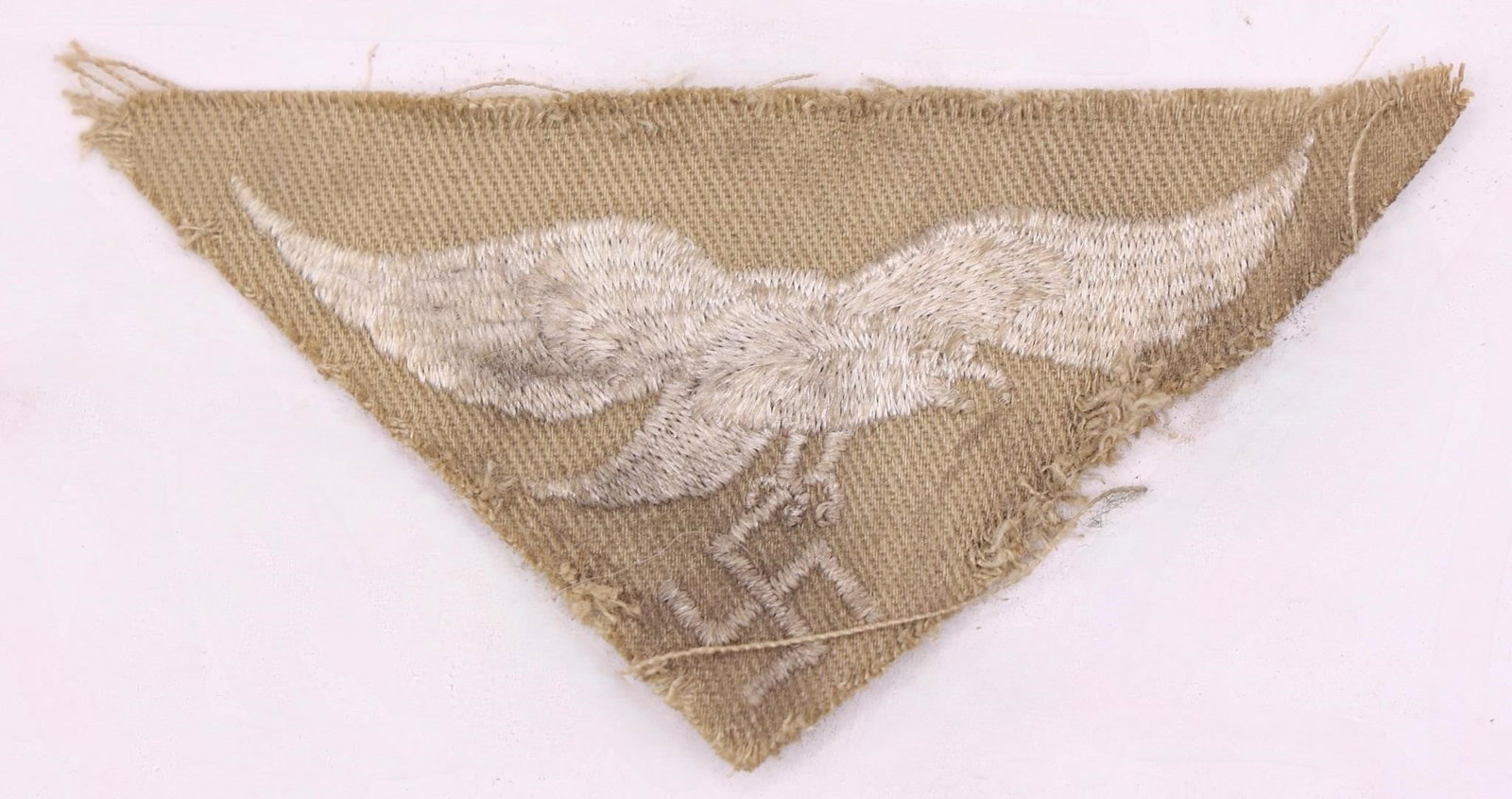 Luftwaffe Africa Corps Tropical Eagle: Machine-embroidered second pattern eagle (circa 1936-1945) in silvery-grey cotton threads on a cut-out, inverted triangular tan cotton base. Measures approximately 83 mm wingspan from tip to tip.