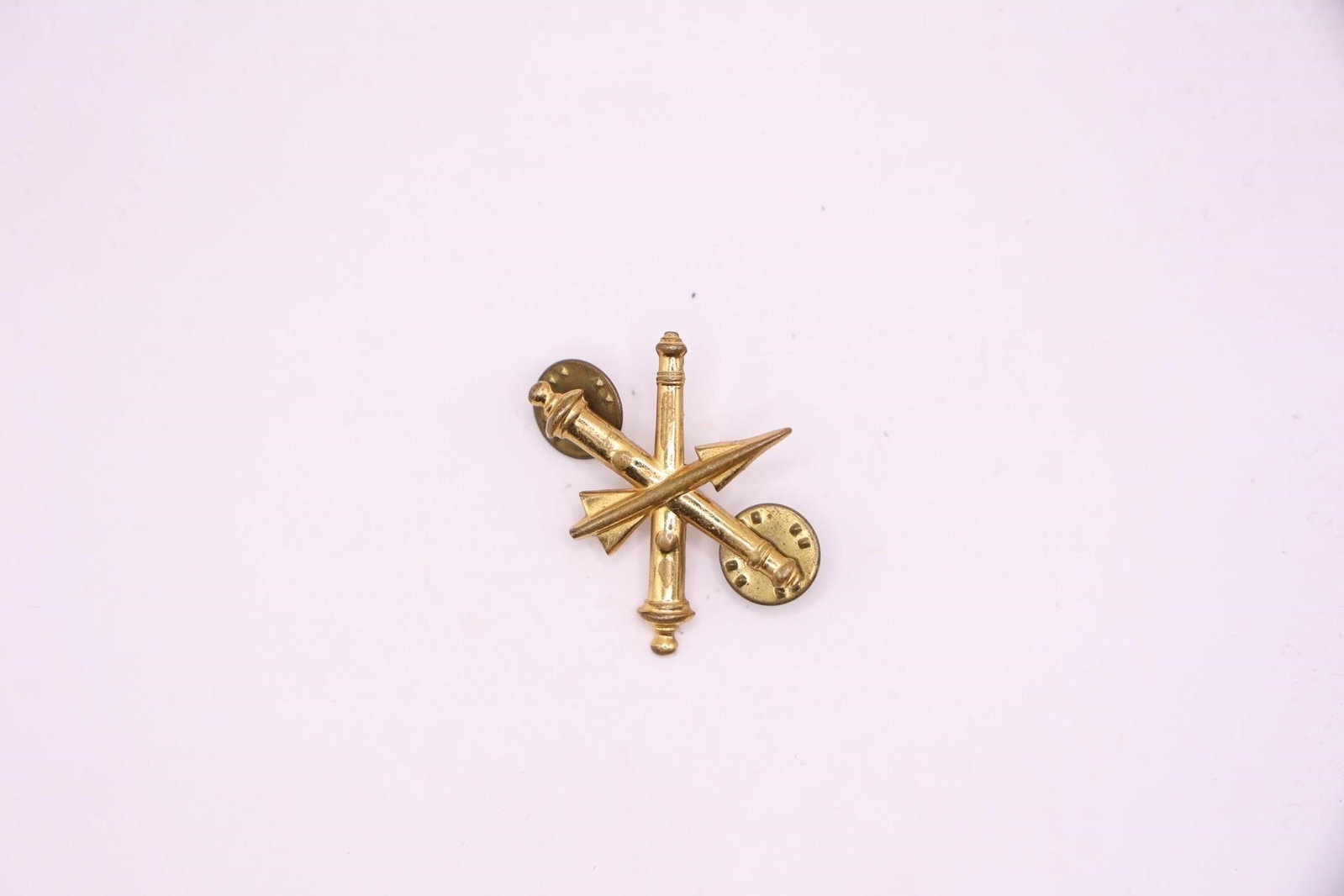 US Army Air Defense Artillery Branch Insignia: It features a missile surmounting two crossed field guns, all in gold-colored metal. The insignia has been in use since 1957, with the Air Defense Artillery established as a basic branch in 1968. It