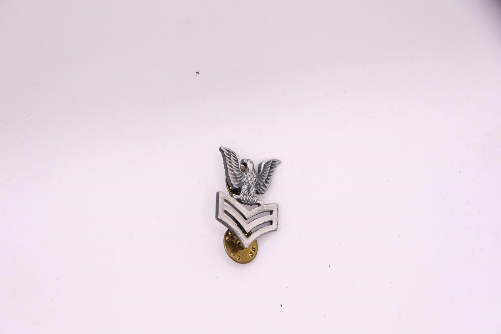 WWII US Navy PO1 E-6 Collar Insignia Pin: The insignia features an eagle with outstretched wings perched above three chevrons. It indicates the rank of Petty Officer First Class in the U.S. Navy. The pin appears to be made of a brushed or