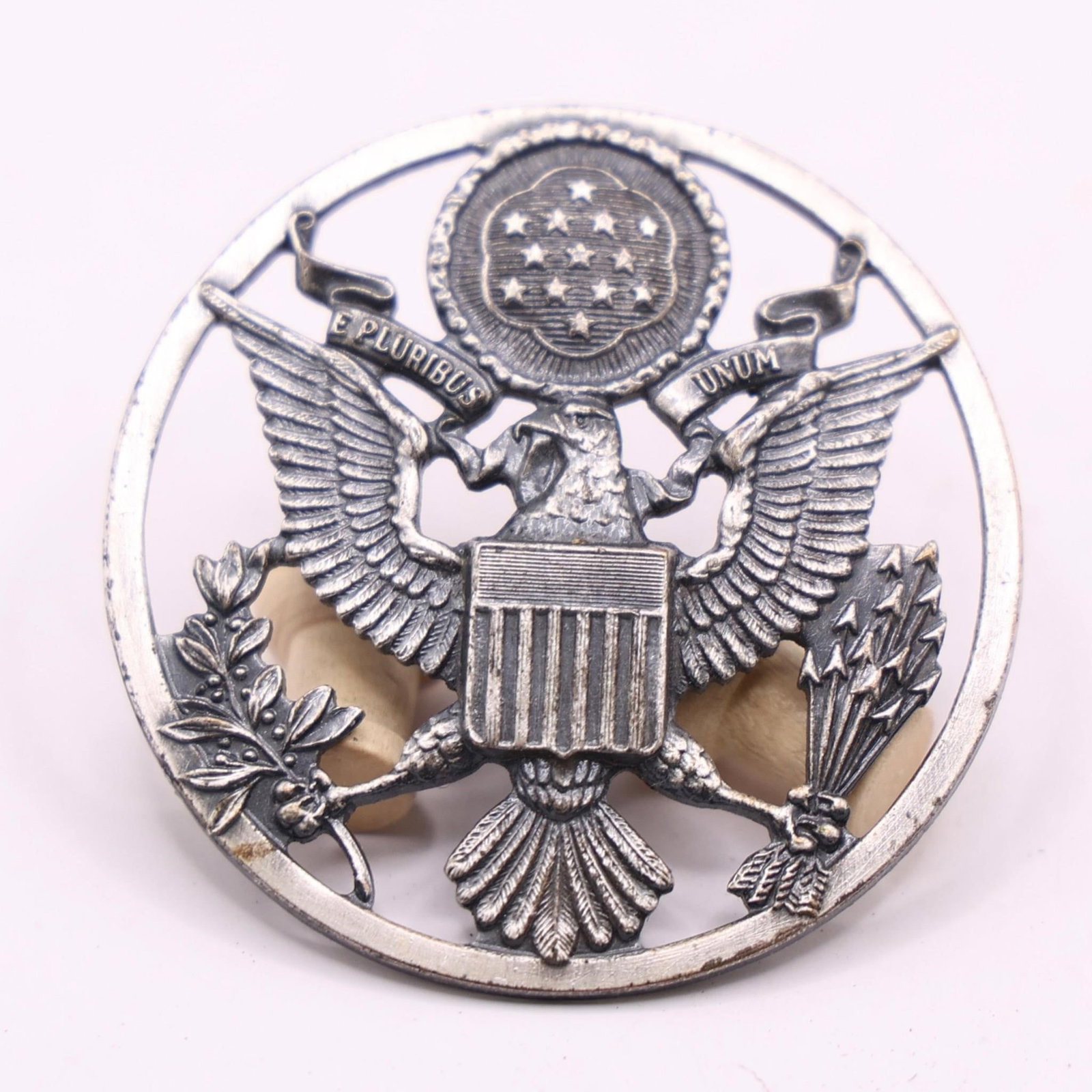 WWII USAF Enlisted Male Service Cap Device: This is a United States Air Force (USAF) enlisted male service cap device. It features the United States Coat of Arms enclosed within a ring. The ring distinguishes it from the officer's version,