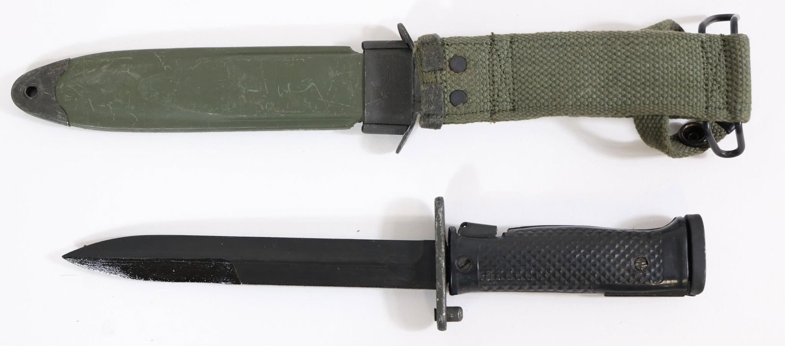 Military-Style Bayonet w/ Scabbard - 11.5" OAL: Military-style bayonet featuring a straight blade, textured black grip scales with rivets, and metal guard with mounting mechanism. Includes olive drab scabbard with canvas hanger and metal fittings. 