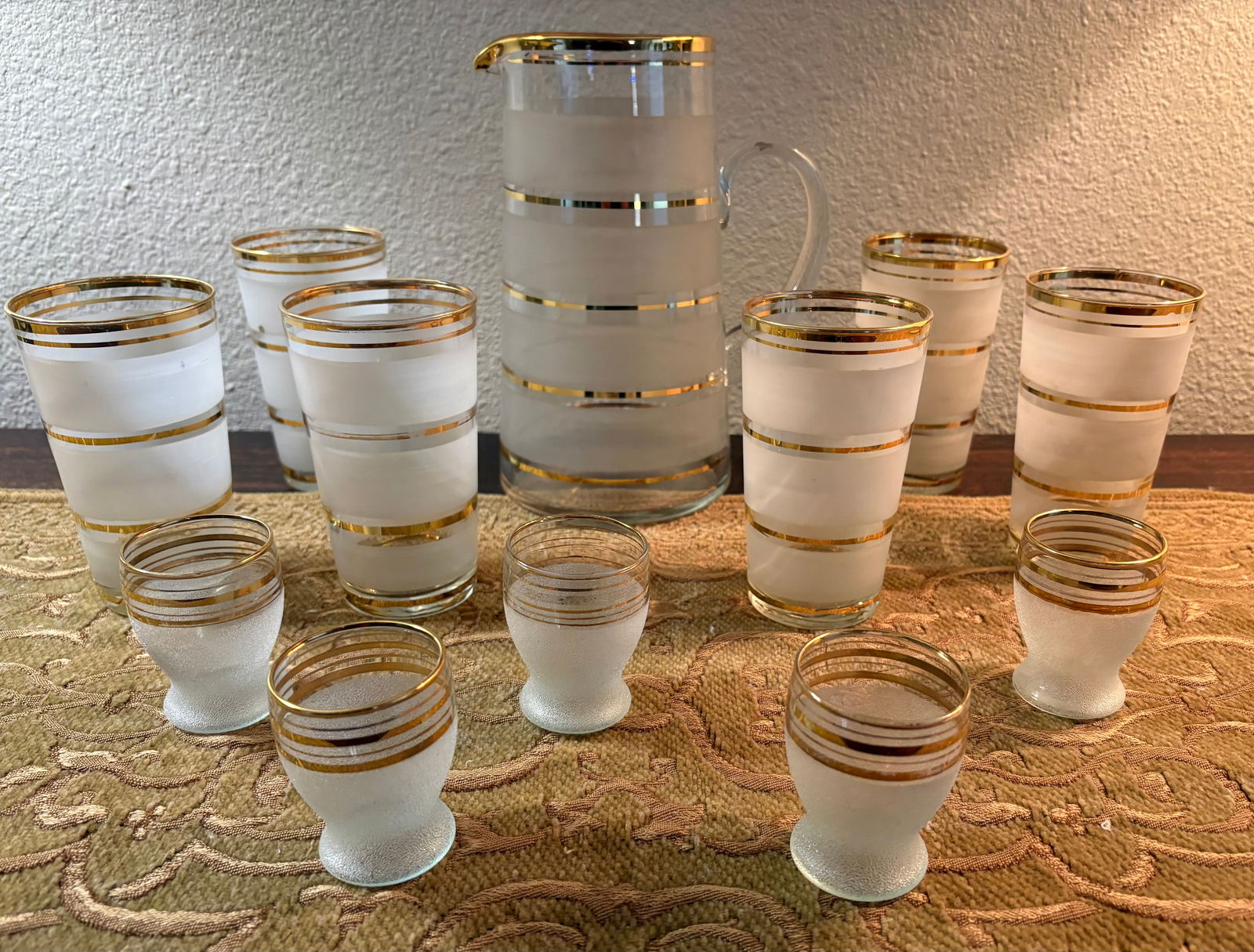 Vintage (1950s-70s) 12-Piece MCM Frosted Glassware: This is a vintage 12-piece set of frosted glassware featuring gold striped accents. This Mid-Century Modern design, from the 1950s-1970s includes a pitcher, 6 tumblers, & 5 shot/juice glasses.Design: