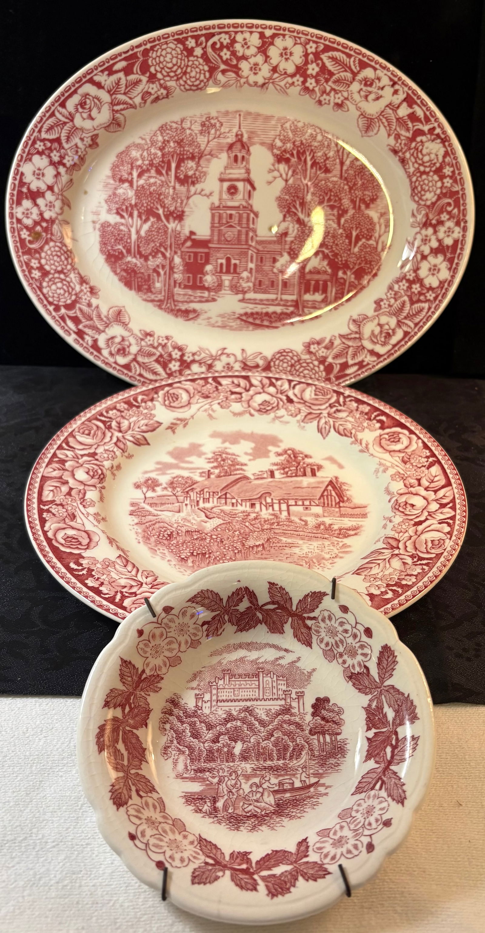 Vintage Red Transferware Pattern Platter, Dinner Plate, & Saucer: This lot features 3 red transferware pieces including one platter, one dinner plate, and one saucer (w/plate hanger).The three pattern designs are as follows:1. Vintage Homer Laughlin oval serving