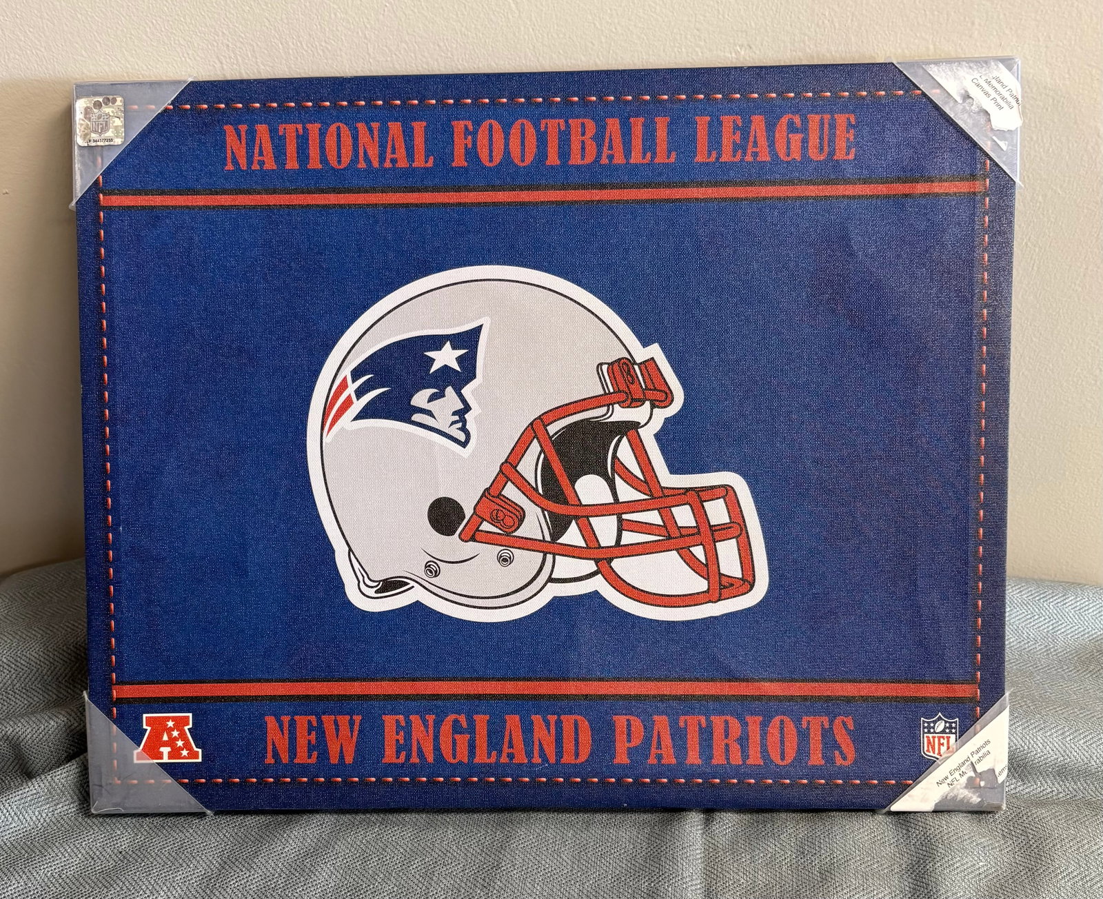 2011 New England Patriots Team Pride Wall Art: This is a wrapped wooden frame / Wall art produced by NFL Properties, LLC, featuring a classic team-colored design with a central display of the Patriots' silver helmet and red facemask. The piece is