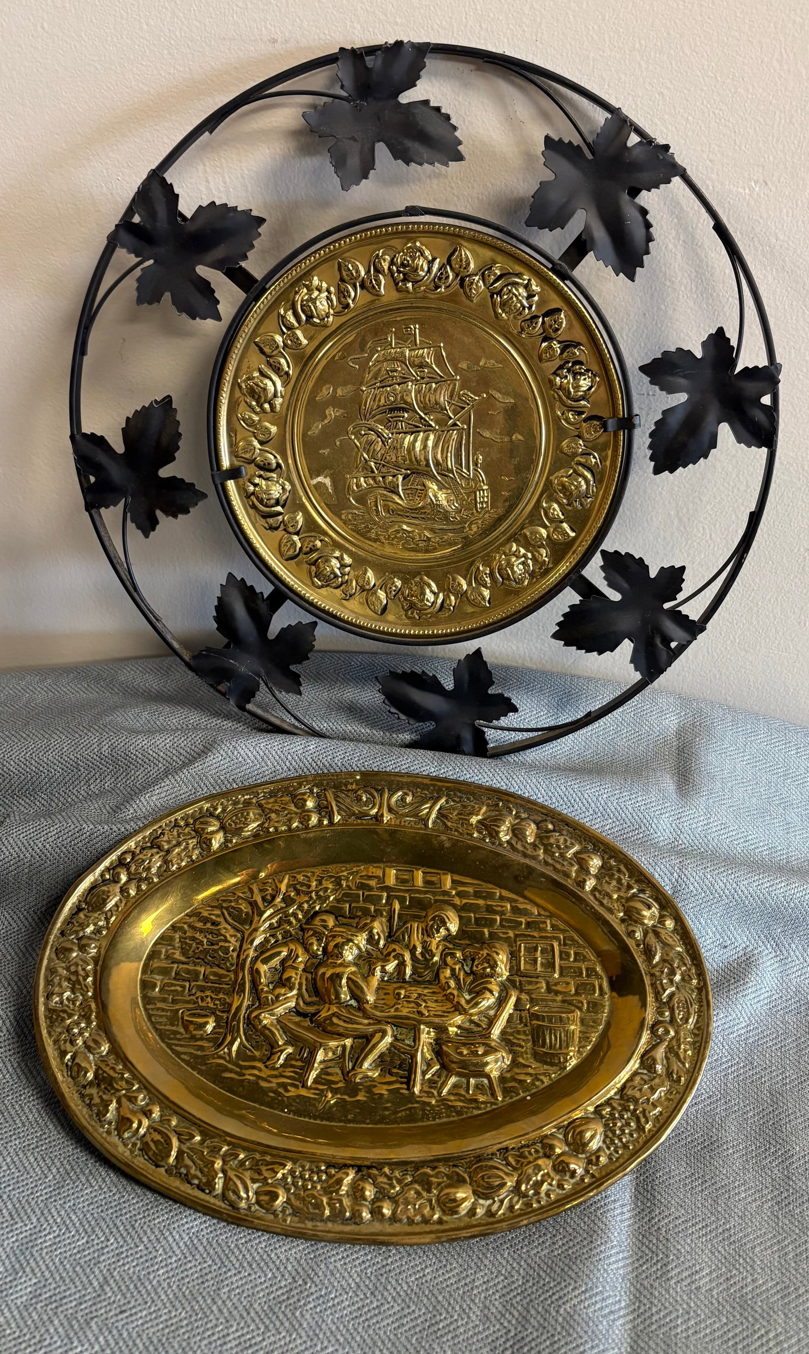 Vintage (1950s/60s) Pair of Embossed English Brass Tavern Plates: A pair of vintage embossed brass wall plaques or "tavern plate". They feature hand-hammered/embossed repoussé scenes from the late 19th or early 20th century. They usually feature an ornate border wi