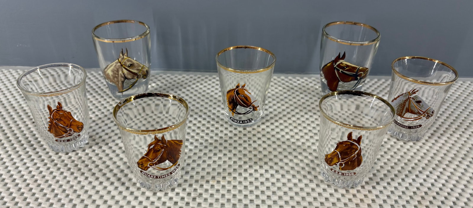 Vtg Grand National / Derby Winners Horse Racing Shot Glass Collection: A collection of vintage Grand National / Derby Winners horse racing shot glasses, likely manufactured during the 1950s or 1960s. Each glass features a detailed, hand-painted style illustration of a le