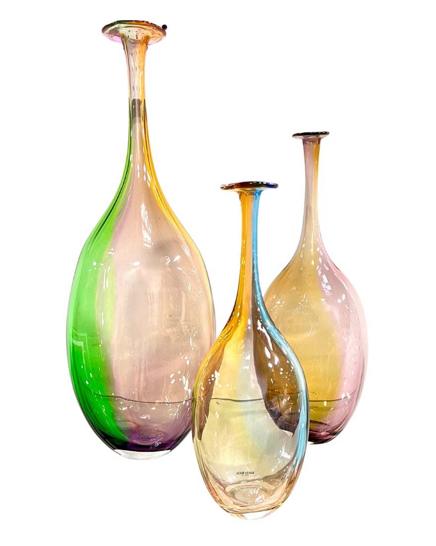 Trio of Kosta Boda Fidji Bottles: A set of three slender-neck bottles in swirling shades of purple, green, blue, yellow, and pink. Small: H 11 1/2", Medium: H 13 7/8", Large: H 17 7/8".