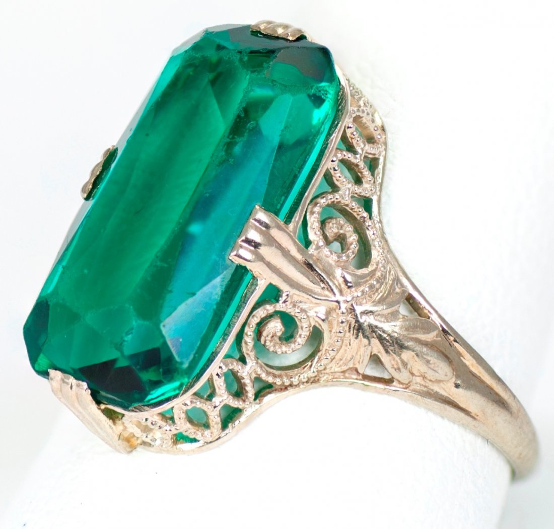 14K White Gold Ring with Simulated Emerald Solitaire: Simulated emerald solitaire set in 14K white gold, and surrounded by filigree. Marked 14K. Size is 5.5 and total ring weight is 0.09 troy ounces.