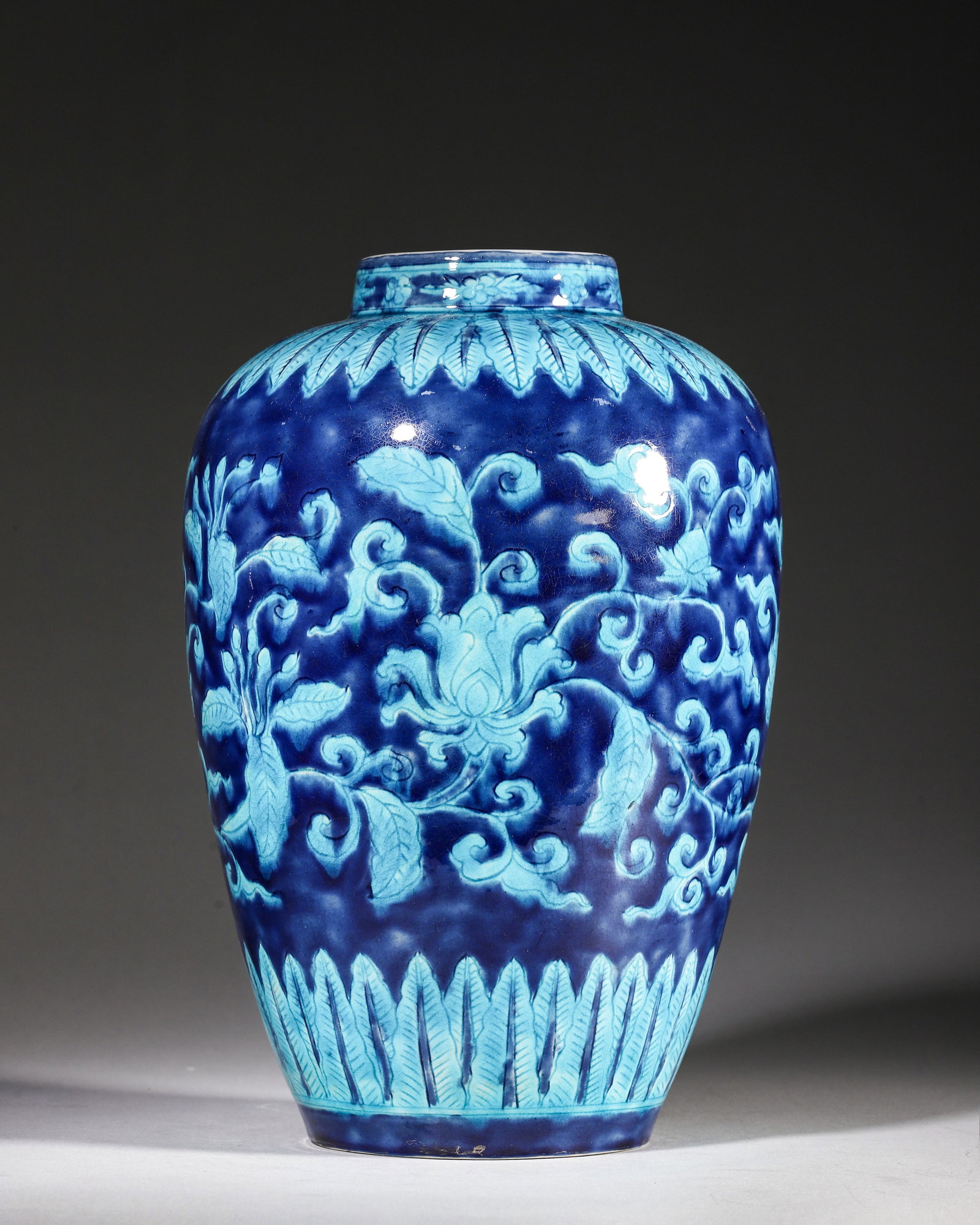 A PEACOCK-GREEN RELIEF FLORAL JAR ON BLUE GROUND, XUANDE PERIOD MING DYNASTY: L 16.5cm (6.5 in); H 24cm (9.45 in),A Ming Xuande porcelain jar with short straight neck and plump shoulder. Relief moulded peacock-green intertwined lotus flowers on deep sapphire blue ground, banana