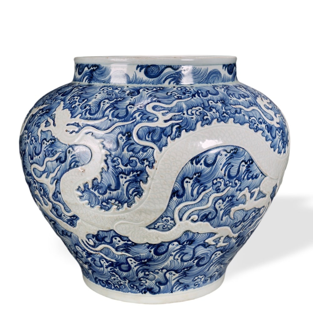 YUAN DYNASTY BLUE AND WHITE CARVED 'WHITE DRAGON AMONG SEA WAVES' JAR: Yuan Dynasty Blue and White Carved 'White Dragon Among Sea Waves' Jar Dimensions: H: 11 3/4 in (30 cm); W: 13 in (33 cm) This robust jar exemplifies one of the most technically virtuosic decorative fo