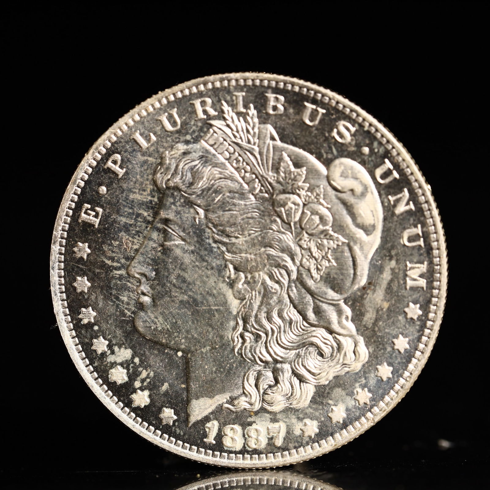 USA Morgan Dollar 1887 Coin: Obv: profile bust with date below and E PLURIBUS UNUM legend and stars around. Rev: eagle with In God we trust above within wreath with UNITED STATES OF AMERICA ONE DOLLAR legend. IN GOD WE TRUST / LI