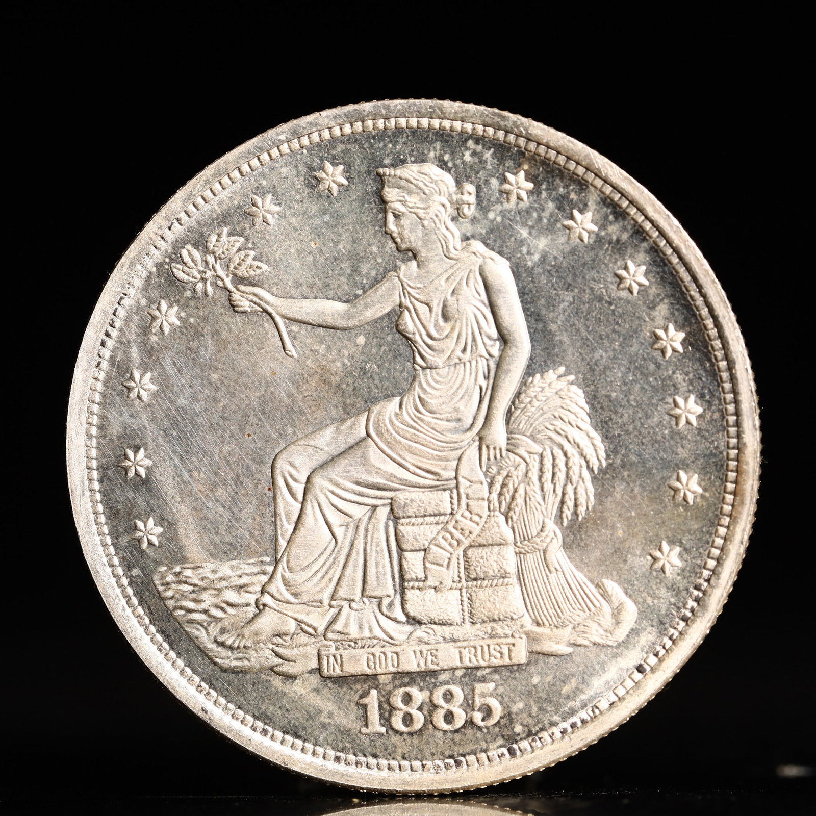 USA Trade Dollar 1885 Coin: American coin. Obverse: Liberty seated on a pedestal facing the sea to the left holding olive branches surrounded by 13 stars. IN GOD WE TRUST / LIBERTY / 1885. Reverse: An eagle holding branches with