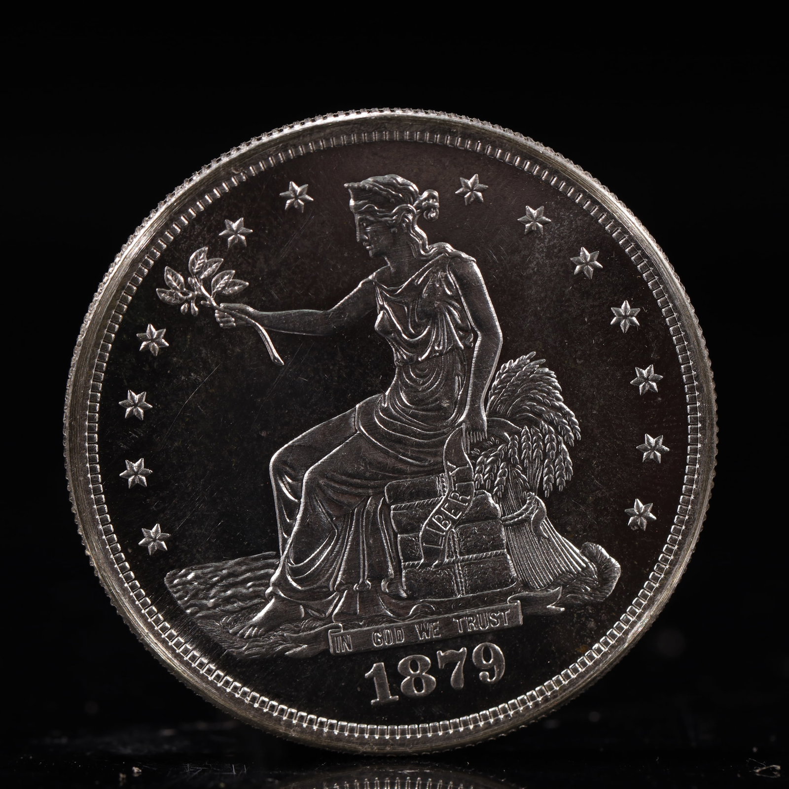 USA Trade Dollar 1879 Coin: American coin. Obverse: Liberty seated on a pedestal facing the sea to the left holding olive branches surrounded by 13 stars. IN GOD WE TRUST / LIBERTY / 1879. Reverse: An eagle holding branches with
